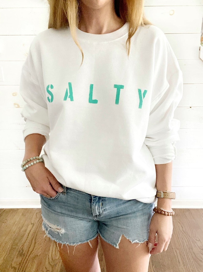 May include: White sweatshirt with the word "SALTY" printed in teal green letters.