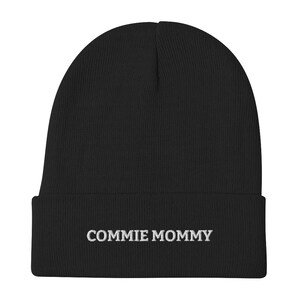 Może przedstawiać: Czarna czapka z dzianiny z haftowanym białym napisem "COMMIE MOMMY" na mankiecie.