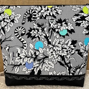 May include: Black and white zippered pouch with a repeating pattern of lemurs and leaves. The pouch has a black bottom with a white stitched design.