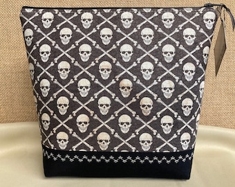 May include: Black zippered pouch with a skull and crossbones pattern. The pouch has a black zipper and a black fabric trim with white stitching.