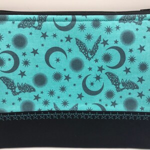 May include: A teal zippered pouch with a black zipper and a black bottom. The pouch has a repeating pattern of bats, moons, and stars on a teal background.