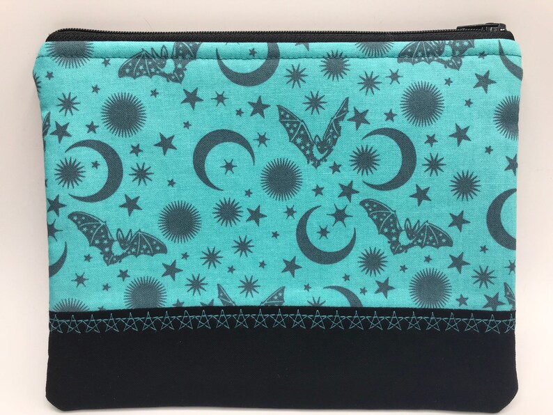 May include: A teal zippered pouch with a black zipper and a black bottom. The pouch has a repeating pattern of bats, moons, and stars on a teal background.