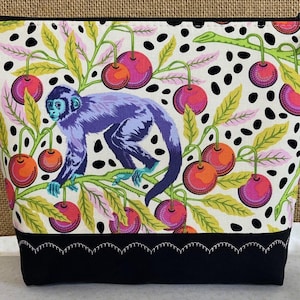 May include: A white zippered pouch with a black and white polka dot background. The pouch features a colorful monkey and cherry design. The pouch has a black fabric bottom with a decorative stitch.