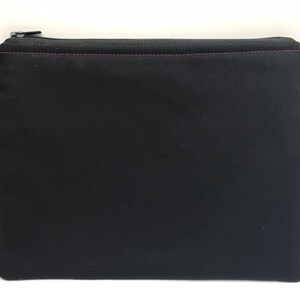 May include: Black zippered pouch with a pink zipper pull. The pouch is made of a soft, black fabric.