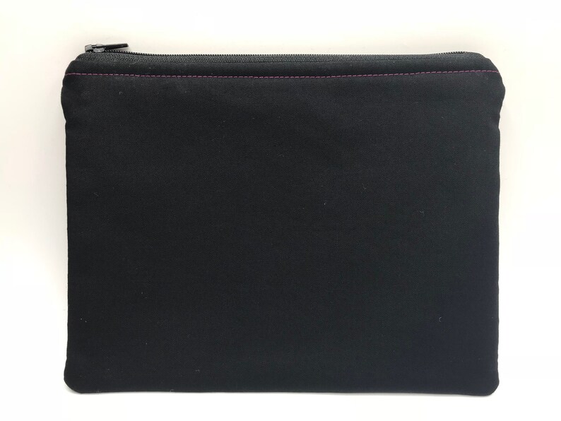 May include: Black zippered pouch with a pink zipper pull. The pouch is made of a soft, black fabric.