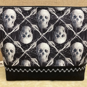 May include: Black zippered pouch with a white skull and crossbones pattern on a black background. The pouch has a black zipper and a black and white stitched trim.