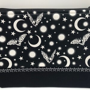 May include: Black zippered pouch with a white crescent moon, stars, and bats pattern. The pouch has a black fabric lining and a white stitched border.