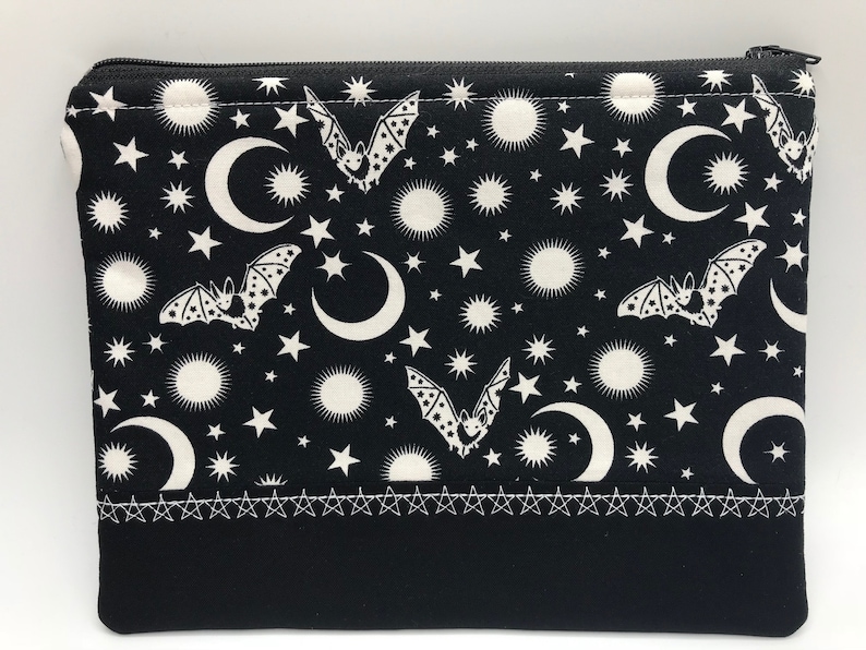 May include: Black zippered pouch with a white crescent moon, stars, and bats pattern. The pouch has a black fabric lining and a white stitched border.