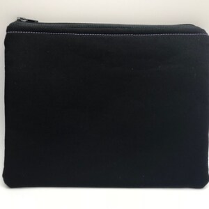 May include: A black zippered pouch with a purple stitch detail. The pouch is made of a soft, fabric material.