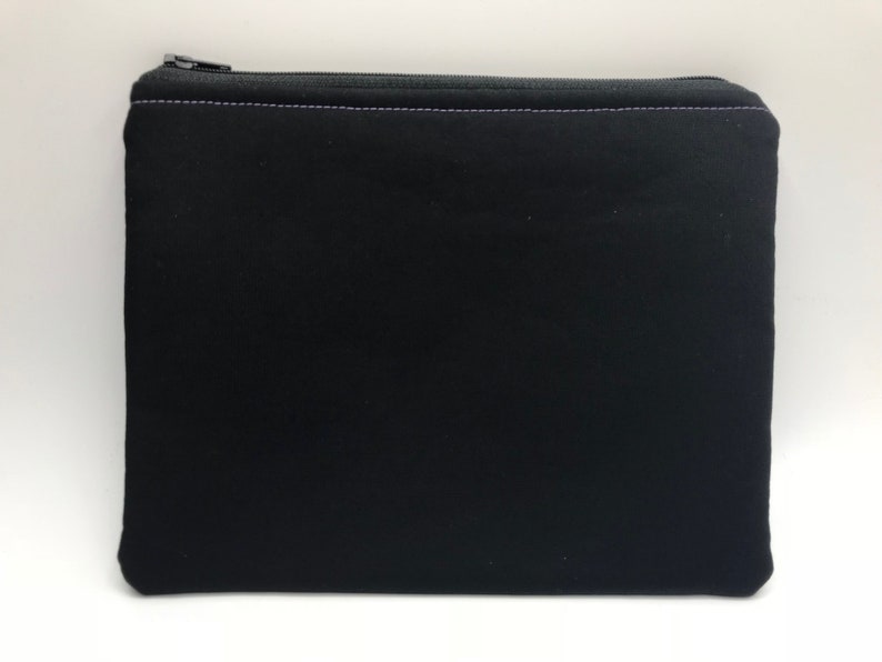 May include: A black zippered pouch with a purple stitch detail. The pouch is made of a soft, fabric material.