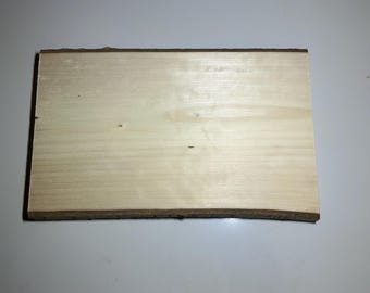 May include: A rectangular wooden plaque with a smooth, light-coloured surface and natural bark edges on the top and bottom. The wood grain is visible across the flat face, showcasing a pale, creamy tone with subtle variations in colour and texture.