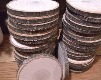 May include: A stack of wooden round slices, each with a natural bark edge. The slices are stacked in two piles, one on top of the other. The wood is a light brown colour and has a smooth surface.