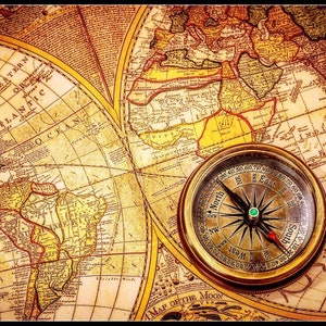 May include: A vintage compass with a gold-colored metal casing and a black needle pointing north. The compass is on top of an old, yellowed map with brown lines and text.