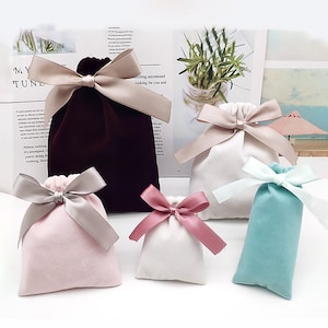 以下が含まれることがあります： さまざまな色のサテンリボンボウが付いたベルベットの巾着袋が5つ。バッグは、ワインレッド、ピンク、白、ライトブルー。リボンはベージュ、ピンク、白です。