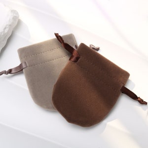 Puede incluir: Dos pequeñas bolsas de terciopelo con cordón de ajuste, una marrón y otra beige, con lazos de cinta de satén marrón a juego.