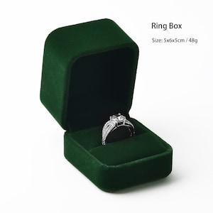 May include: A dark green velvet ring box with an open lid, revealing a silver ring with a large, clear center stone. The box is square, with rounded corners. Text on the image reads "Ring Box" and "Size: 5x6x5cm / 48g".