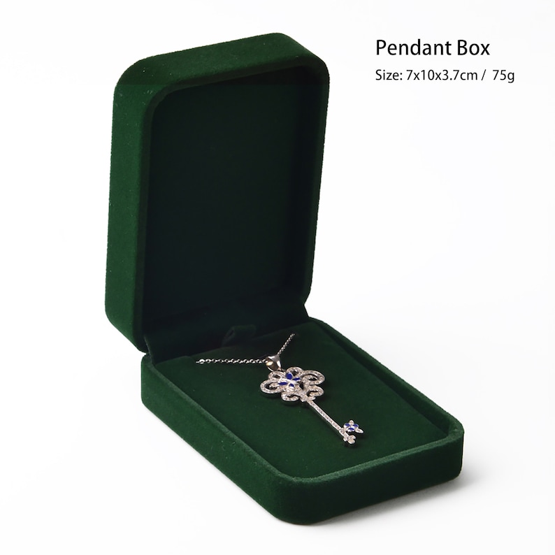 May include: Open, dark green velvet pendant box with a silver key-shaped necklace. The necklace has a floral design with blue accents. The box is rectangular with rounded corners.