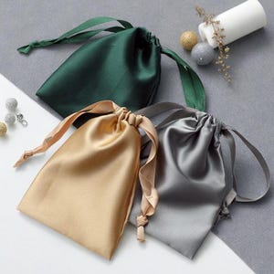 May include: Three satin drawstring bags in green, gold, and gray. The bags are made of soft, silky fabric and have a luxurious feel.