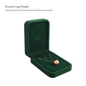 May include: A gold necklace with a large, round, peach-colored pendant rests inside an open, dark green velvet jewelry box. The box has the words "Great Material" printed inside. The text "Custom Logo Sample" is above the box.