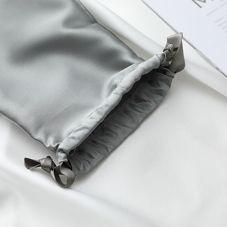 May include: A gray satin drawstring bag with a gray ribbon tie. The bag is made of soft, luxurious fabric and is perfect for storing small items.