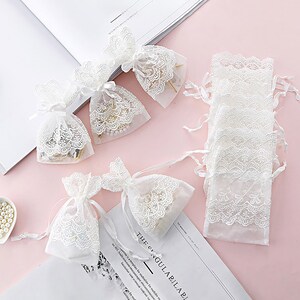 May include: White lace drawstring bags with delicate embroidery. The bags are perfect for packaging small gifts or favors.