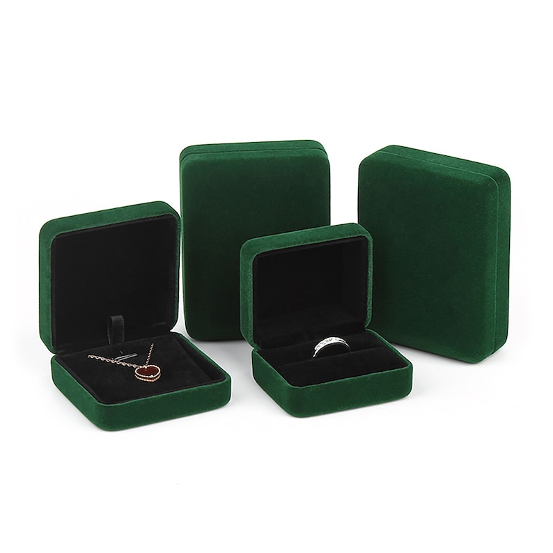 May include: Four green velvet jewelry boxes of different sizes. The largest box is on the right, and the smallest box is on the left. The smallest box has a necklace inside, and the second smallest box has a ring inside.
