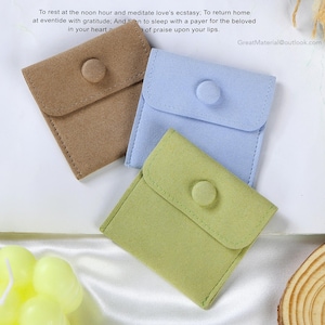 May include: Three small, square, fabric pouches with button closures. The pouches are brown, light blue, and green.