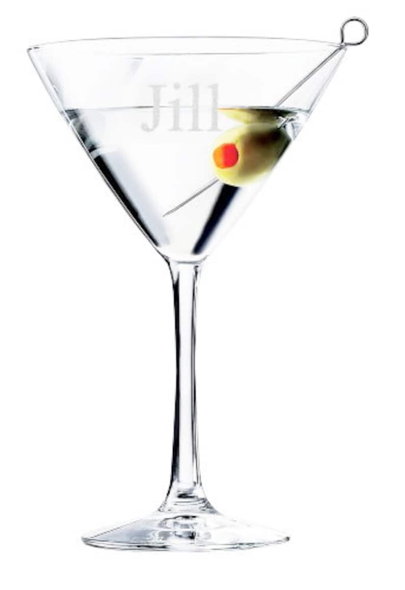 Puede incluir: Una copa de martini de vidrio transparente con una aceituna verde y un palillo de c&oacute;ctel. La copa est&aacute; grabada con el nombre "Jill".