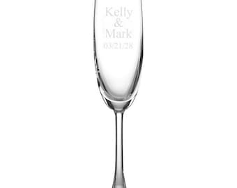 Può includere: Un flûte da champagne trasparente con un lungo stelo e una coppa larga. Il testo "Kelly & Mark" e la data "03/21/28" sono incisi sul vetro. Il bicchiere è posto su uno sfondo bianco.