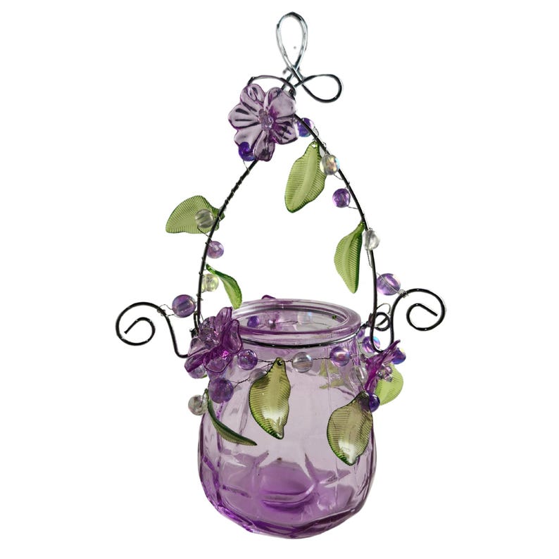 Pu&ograve; includere: Un portacandele sospeso in vetro con una tonalit&agrave; viola. Il supporto &egrave; decorato con fiori viola, foglie verdi e perline trasparenti. La struttura metallica presenta un design a spirale decorativo.