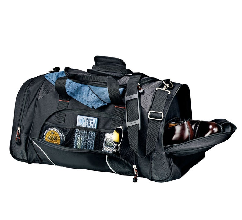 Puede incluir: Bolsa de viaje de lona negra con m&uacute;ltiples bolsillos y un compartimento para zapatos. La bolsa est&aacute; abierta y muestra una toalla azul, gafas de sol, un mando a distancia y un peque&ntilde;o recipiente de bet&uacute;n para zapatos en el interior.