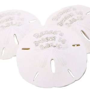 May include: Three white sand dollar favors with the text "Renee's Sweet 16 8.26.19" engraved on each.