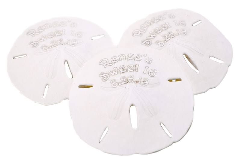 May include: Three white sand dollar favors with the text "Renee's Sweet 16 8.26.19" engraved on each.