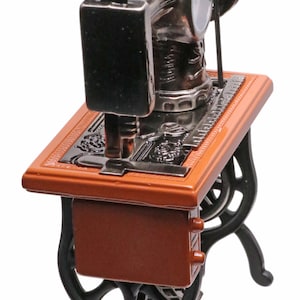 Peut inclure: Une machine &agrave; coudre miniature avec une base en bois brun et des pieds en m&eacute;tal noir. La machine a un corps en m&eacute;tal argent&eacute; et une aiguille en m&eacute;tal noir.