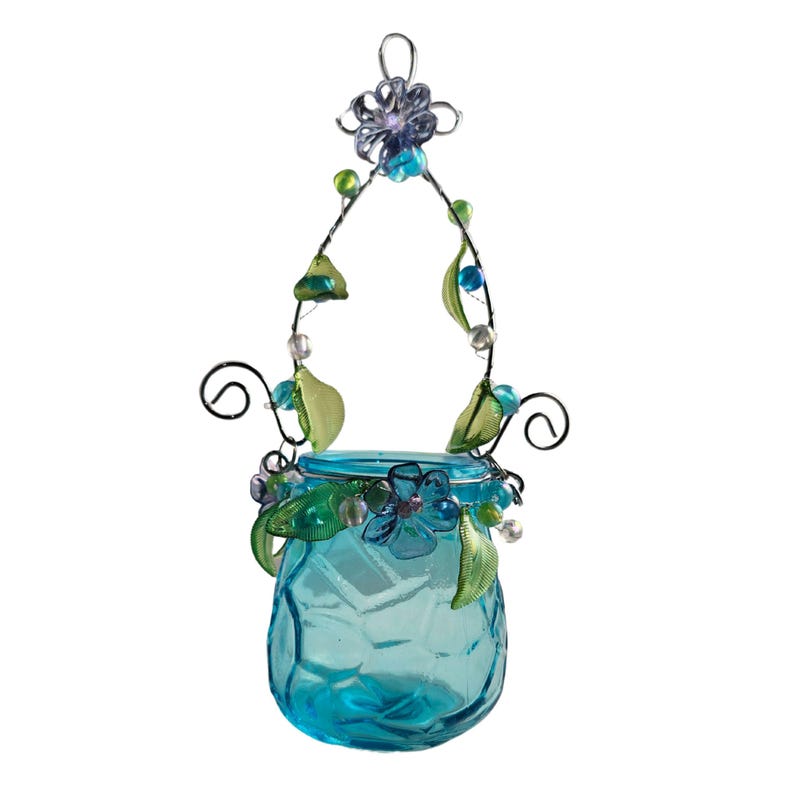 Pu&ograve; includere: Un barattolo di vetro turchese sospeso con un manico decorativo in filo di ferro. Il barattolo &egrave; adornato con fiori blu, foglie verdi e perline. Il manico in filo di ferro &egrave; impreziosito da perline verdi e blu e un fiore in cima.
