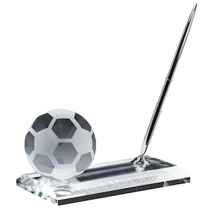 Pu&ograve; includere: Portapenne da scrivania in cristallo con un pallone da calcio in vetro smerigliato e una penna argentata. La base &egrave; incisa con il testo "Coach Mark Wilson".