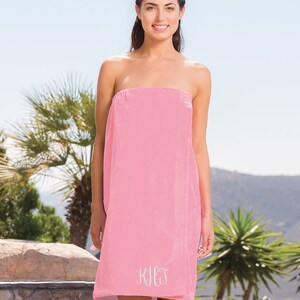 May include: Pink wrap towel with a white monogram "K.H.J." embroidered on the front.