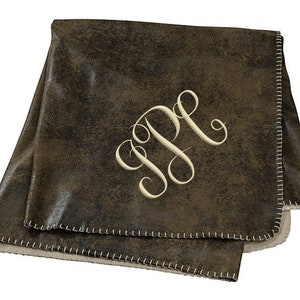 May include: A brown faux leather throw blanket with a white embroidered monogram "JP". The blanket has a white sherpa lining and a stitched edge.