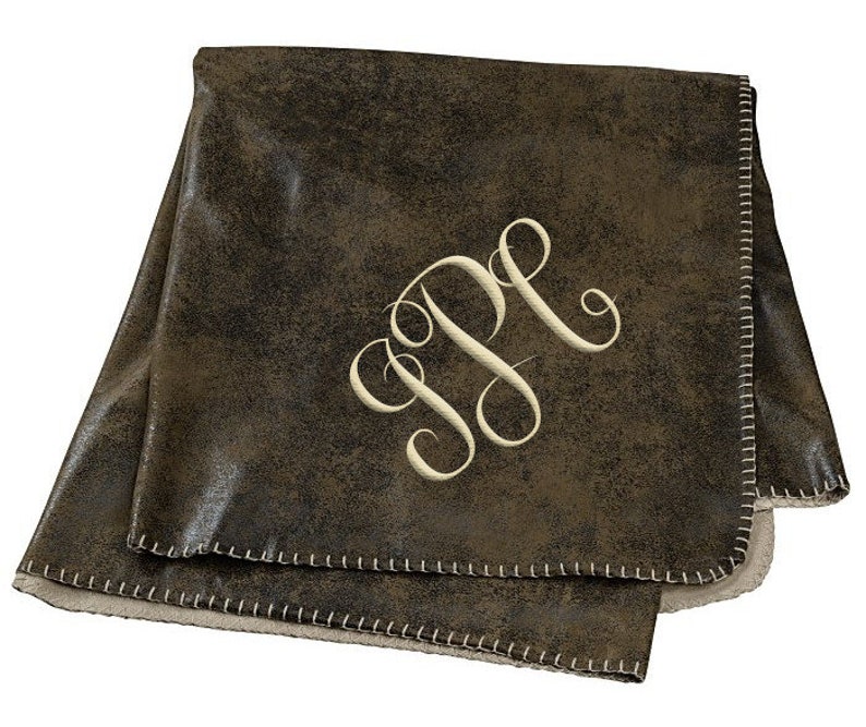 May include: A brown faux leather throw blanket with a white embroidered monogram "JP". The blanket has a white sherpa lining and a stitched edge.