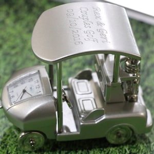 May include: Silver golf cart clock with a personalized inscription that reads "Rex & Geri Couples Golf 09/10/2016".