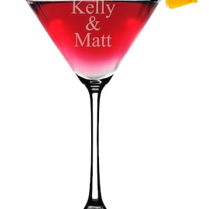 May include: A clear glass martini glass with a red cocktail and an orange slice garnish. The glass is engraved with the text "Kelly & Matt".