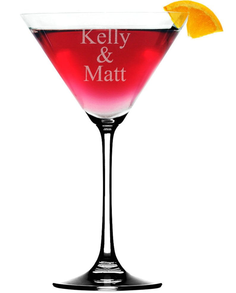 Puede incluir: Una copa de martini de vidrio transparente con un c&oacute;ctel rojo y una rodaja de naranja como guarnici&oacute;n. La copa est&aacute; grabada con el texto "Kelly & Matt".