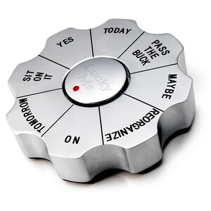 May include: A silver-colored, eight-sided, spinning wheel with the words "Yes", "No", "Maybe", "Today", "Tomorrow", "Sit on It", "Pass the Buck", and "Reorganize" printed on each side. The wheel has a red dot in the center and the words "Lucky Me" printed on the center button.