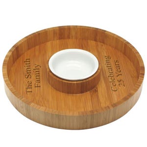 May include: A round wooden serving tray with a small white ceramic bowl in the center. The tray is engraved with the text "The Smith Family Celebrating 25 Years".