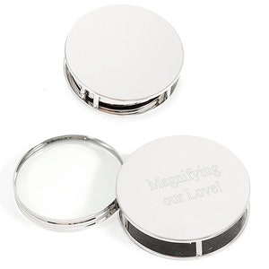 May include: A silver magnifying glass with a round handle and a clear lens. The handle has the inscription "Magnifying our Love!" engraved on it.