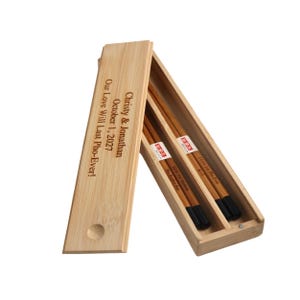 May include: A set of wooden chopsticks in a bamboo box with a personalized message that reads "Christy & Jonathan October 1, 2027 Our Love Will Last Pho-Ever!"