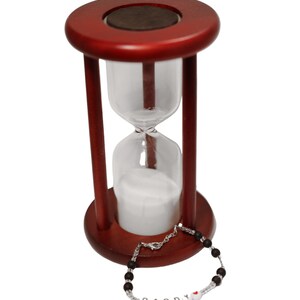 K&ouml;nnte beinhalten: Eine Sanduhr aus Holz mit wei&szlig;em Sand und einem schwarzen Perlenarmband mit dem Wort "DADDY" in wei&szlig;en Perlen mit einer roten Herzperle.