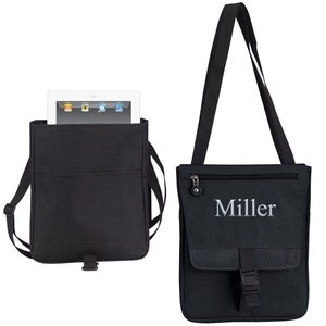 May include: Black canvas messenger bag with a zippered pocket and a buckle closure. The bag has a strap and is shown with a tablet inside. The bag is personalized with the name "Miller" in silver embroidery.