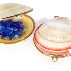 May include: Two clam shell boxes with gold trim. One box is open and contains blue beads. The other box is closed and has the inscription "Mandy & Kevin March 21, 2033".