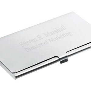 May include: A silver metal business card holder with the engraved text "Steven R. Marshall Director of Marketing".
